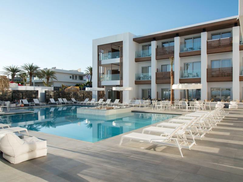 Modern hotelzwembad met ligstoelen en palmbomen onder een heldere hemel.