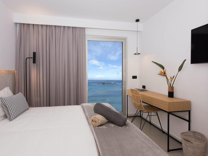 Modern hotelkamer met zeezicht, groot bed en bureau met decoratieve planten.