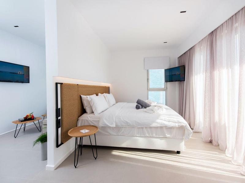 Lichte, moderne slaapkamer met groot bed, raam met gordijnen en wand-tv.