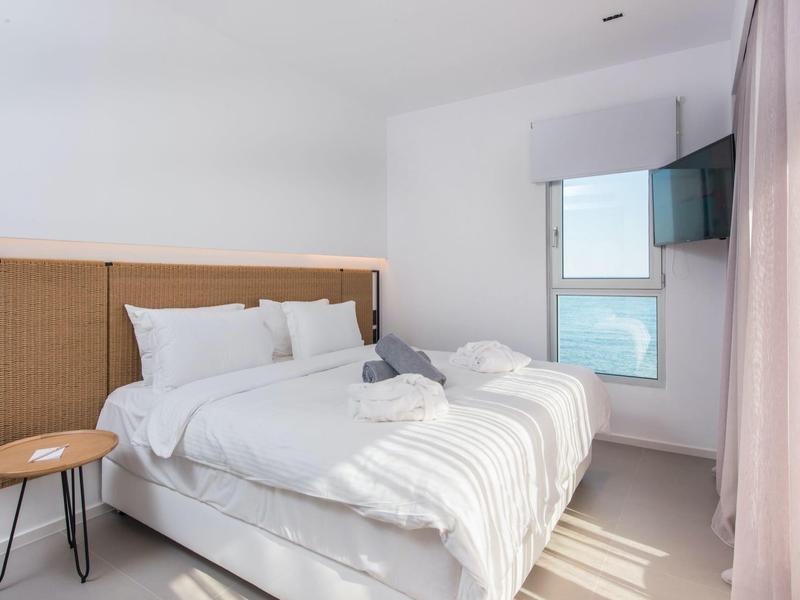 Moderne, lichte slaapkamer met tweepersoonsbed, raam en klein bijzettafeltje.