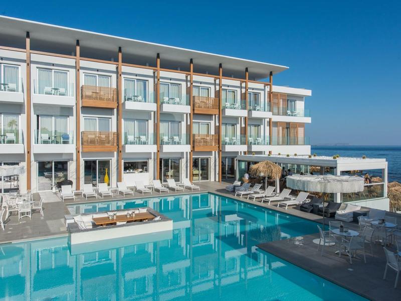 Modern hotel met groot zwembad en zeezicht onder een heldere hemel.