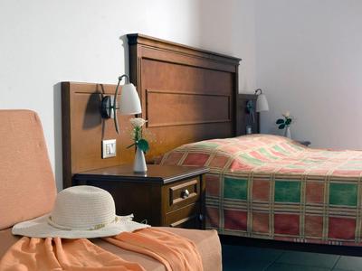 Ein schlichtes Hotelzimmer mit einem Bett in buntem Karo-Design und einem Stuhl mit Hut.