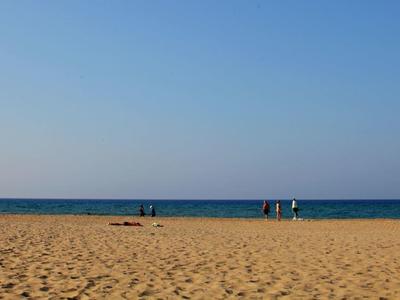Strand mit Sand, einem Rettungsturm links und ruhigem Meer im Hintergrund unter klarem Himmel.
