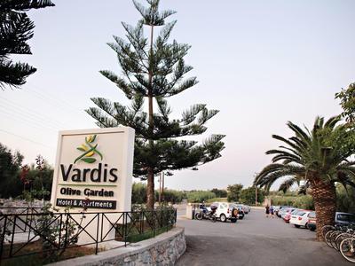 Parkplatz mit Autos neben einem Garten und einem Schild mit der Aufschrift 'Vardis Olive Garden'