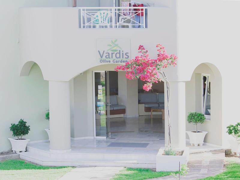 Hoteleingang mit weißer Fassade, pink blühendem Baum und grünen Pflanzen in Töpfen