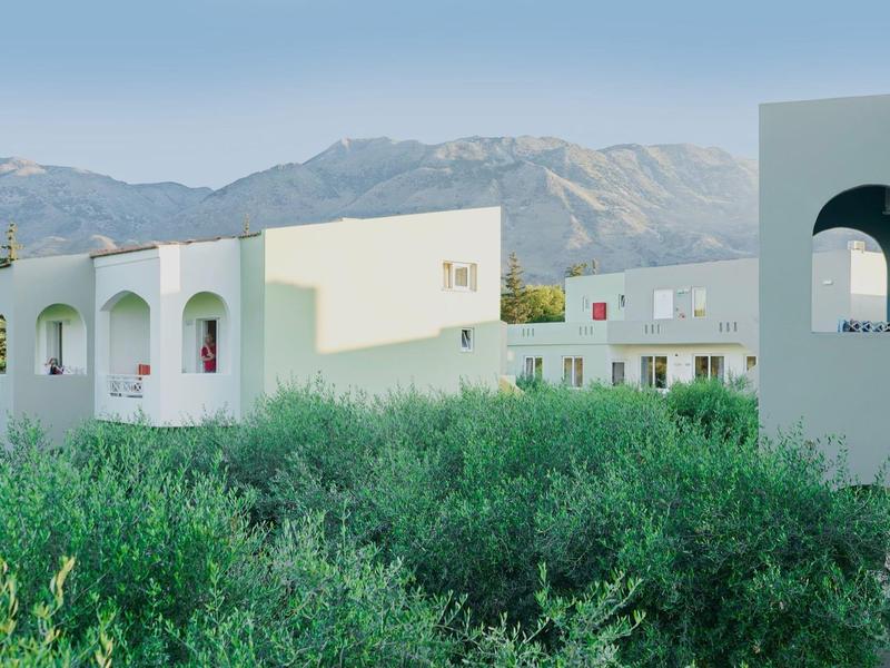 Hotelgebäude vor Bergen mit grüner Vegetation im Vordergrund bei klarem Himmel