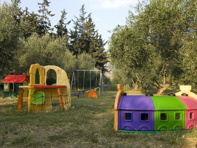 Kinderspielplatz mit buntem Spielhaus, Rutsche, Schaukeln und umgeben von Bäumen auf Wiese.
