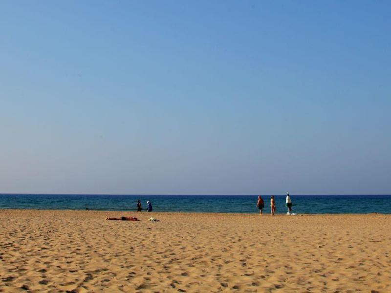 Strand mit Sand, einem Rettungsturm links und ruhigem Meer im Hintergrund unter klarem Himmel.