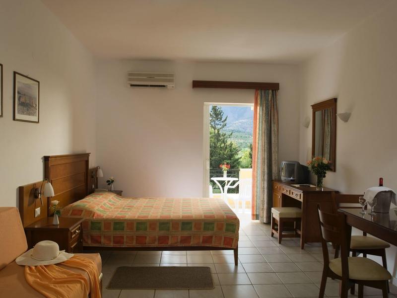 Helles Hotelzimmer mit Doppelbett, Stühlen und Blick auf einen Balkon mit grünem Ausblick.