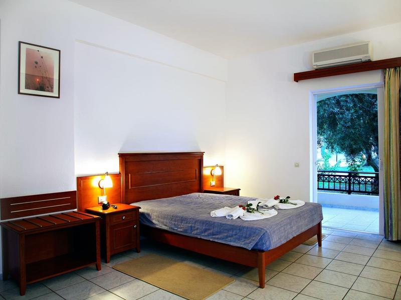 Hotelzimmer mit Doppelbett, Nachttischen, Lampen und offenem Balkon mit Blick ins Grüne.