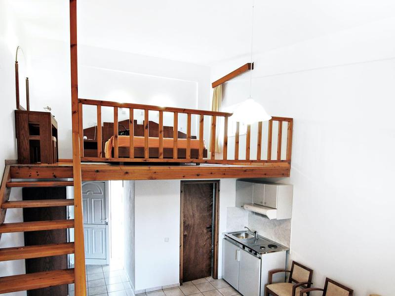 Kleines Apartment mit Holzloftbett, Kochnische und Sitzbereich unter dem Hochbett.