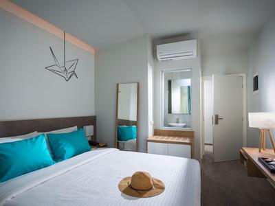 Camera d'hotel moderna con letto matrimoniale, cuscini blu, specchio e lampada elegante.