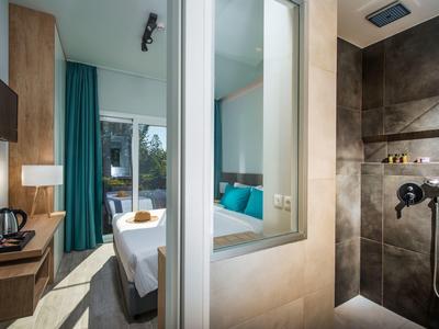 Camera d'hotel moderna con letto matrimoniale, scrivania e doccia piastrellata aperta.