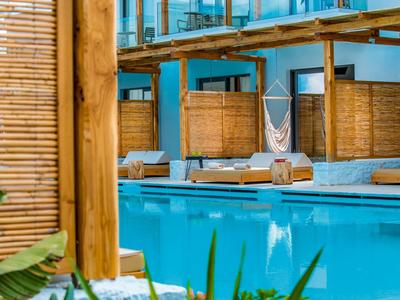 Piscina azzurra con lettini in legno e amaca in un ambiente vacanziero rilassante.