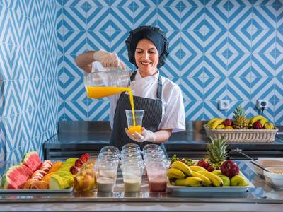 Köchin gießt frisch gepressten Saft hinter einem Buffet mit Obst und Getränken.