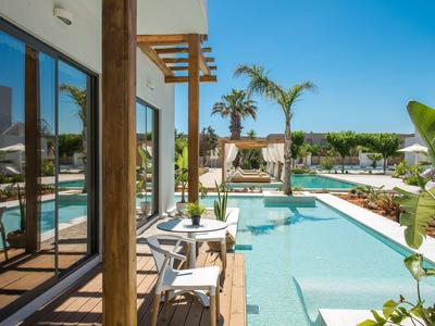 Piscina all'aperto con sedie, tavoli, piante e cielo azzurro.