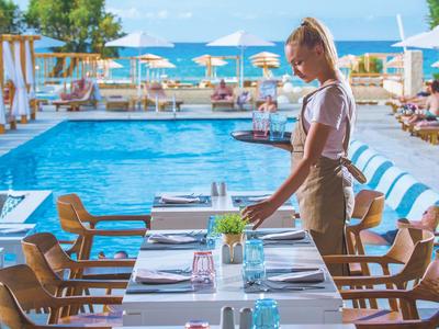 Frau am gedeckten Tisch vor einem Pool mit Blick aufs Meer und Sonnenschirme.