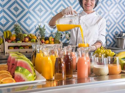 Un cameriere versa succo d'arancia fresco in un bicchiere tra varie bevande al buffet.