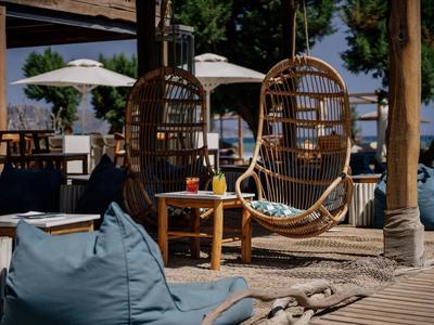 Area esterna dell'hotel con sedie sospese in vimini e cuscini blu vicino all'acqua.