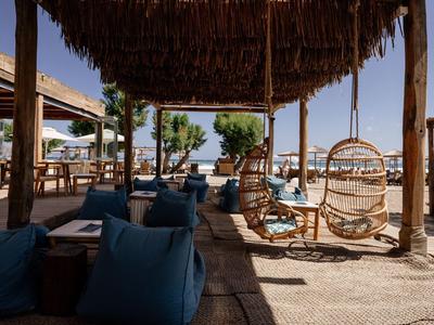 Terrazza ombreggiata con sedie sospese e pouf blu di fronte al mare.