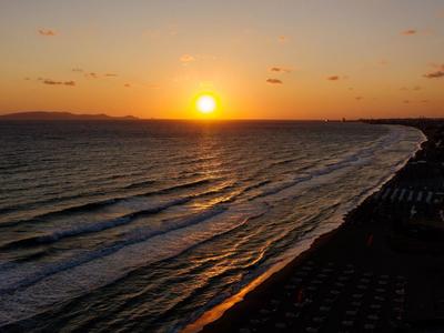 Tramonto dorato su una spiaggia con onde e cielo parzialmente nuvoloso.