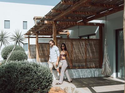 Coppia cammina davanti a una terrazza con pergolato in legno, casa moderna sullo sfondo.