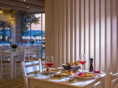 Tavolo da ristorante con pasto, vino rosso e vista sul mare al tramonto.
