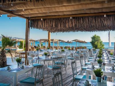 Terrazza di un ristorante sul mare con tavoli bianchi e ombrelloni di paglia.