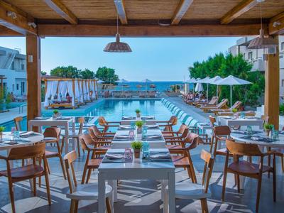 Offener Essbereich mit Holzdach, Tischen und Stühlen neben großem Pool mit Blick aufs Meer.