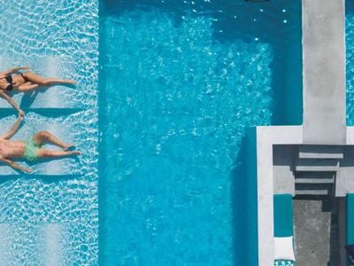 Zwei Frauen entspannen in einem Pool mit Liegestühlen und Sonnenliegen neben dem Wasser.