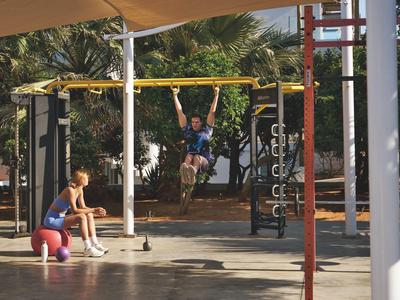 Zwei Kinder spielen an einem Kletter- und Spielgerüst im Freien bei sonnigem Wetter.