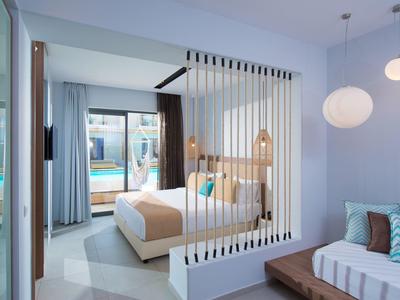 Camera d'hotel moderna con letto, divano e vista sulla piscina attraverso una porta scorrevole in vetro.