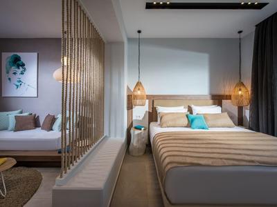 Camera d'hotel moderna con letto matrimoniale, divano e luci sospese.