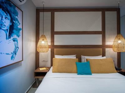 Camera d'hotel moderna con letto matrimoniale, cuscini colorati e lampade a sospensione in vimini.