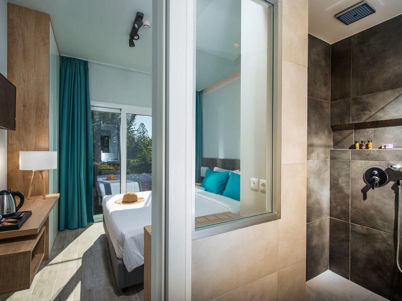 Camera d'hotel moderna con letto matrimoniale, scrivania e doccia piastrellata aperta.