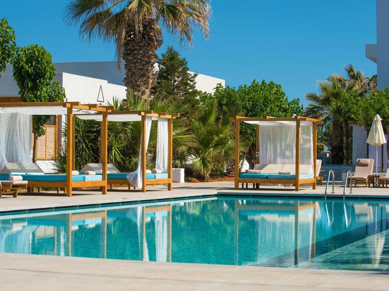 Piscina dell'hotel con gazebi in legno e palme sotto un cielo azzurro.