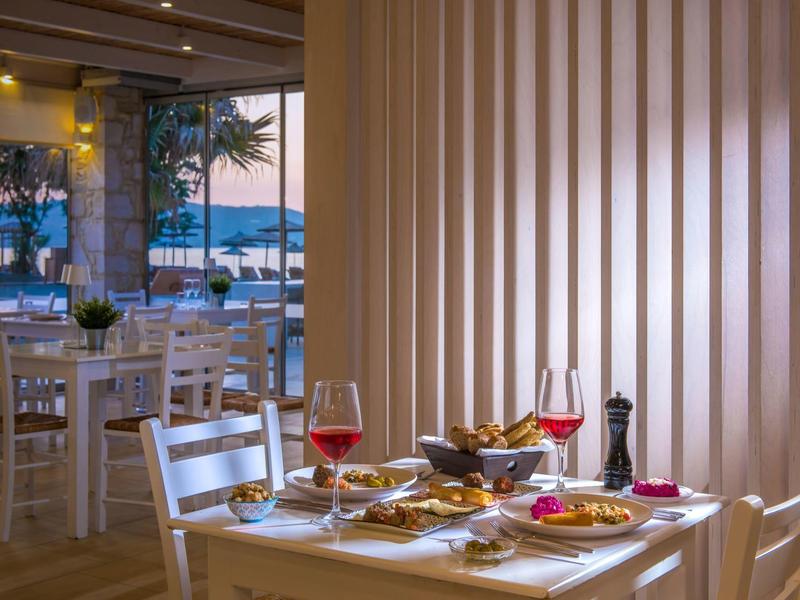 Tavolo elegante apparecchiato con vino rosato in un ristorante con vista mare al tramonto.