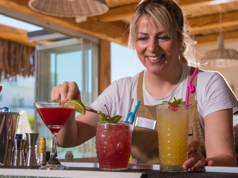 Una donna prepara cocktail colorati in un bar con travi in legno.