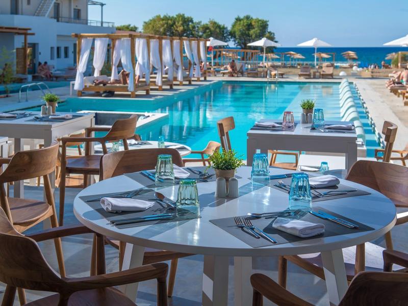 Terrazza del ristorante con piscina, tavoli rotondi, sedie in legno e ombrelloni bianchi.