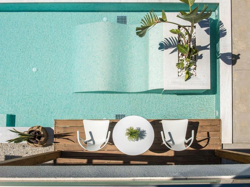 Terrazza in legno con tavolo rotondo e due sedie accanto a una piscina turchese.