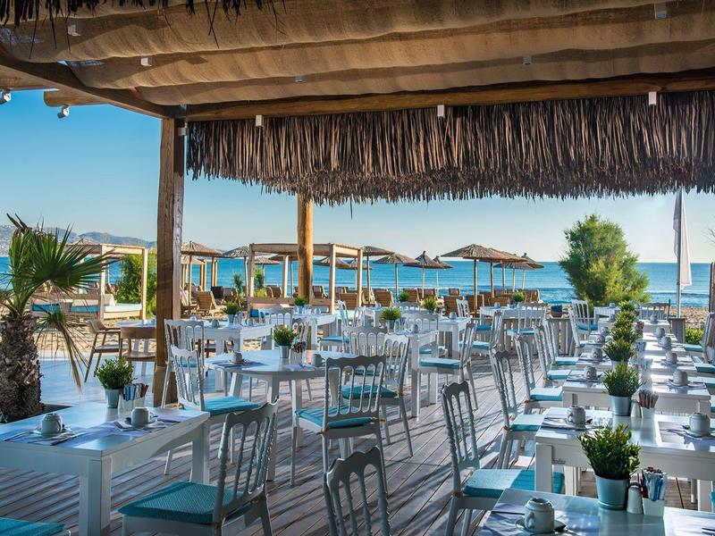 Terrazza di ristorante sul mare con tavoli bianchi e ombrelloni di paglia.