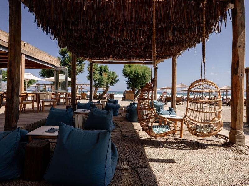 Terrazza ombreggiata con sedie sospese e pouf blu di fronte al mare.
