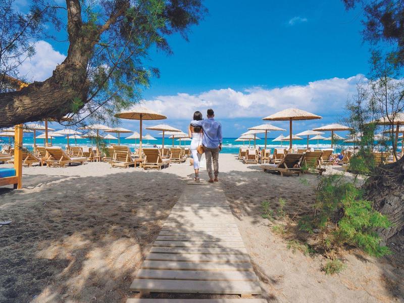 Coppia cammina verso una spiaggia con ombrelloni sotto un cielo sereno.