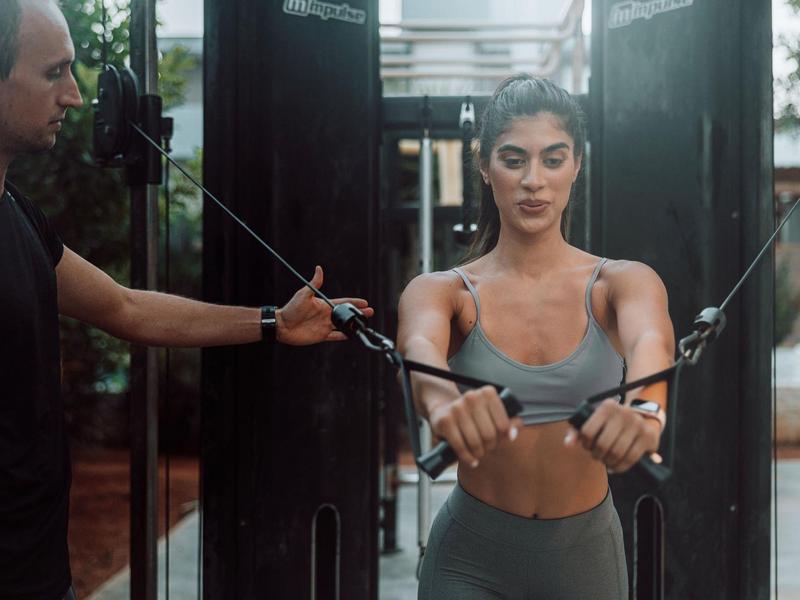 Una donna si allena con cavi da palestra, assistita da un allenatore.