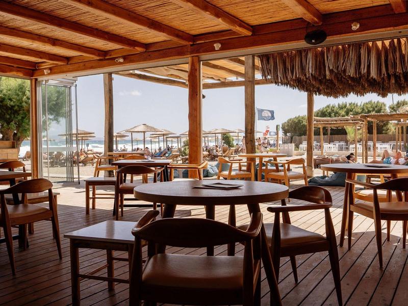 Terrazza di un ristorante in legno con vista sulla spiaggia, tavoli e sedie disposti.
