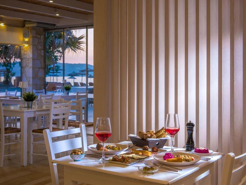 Tavolo da ristorante con pasto, vino rosso e vista sul mare al tramonto.