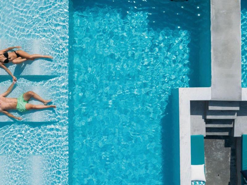 Due donne si rilassano in una piscina moderna con lettini e scala.