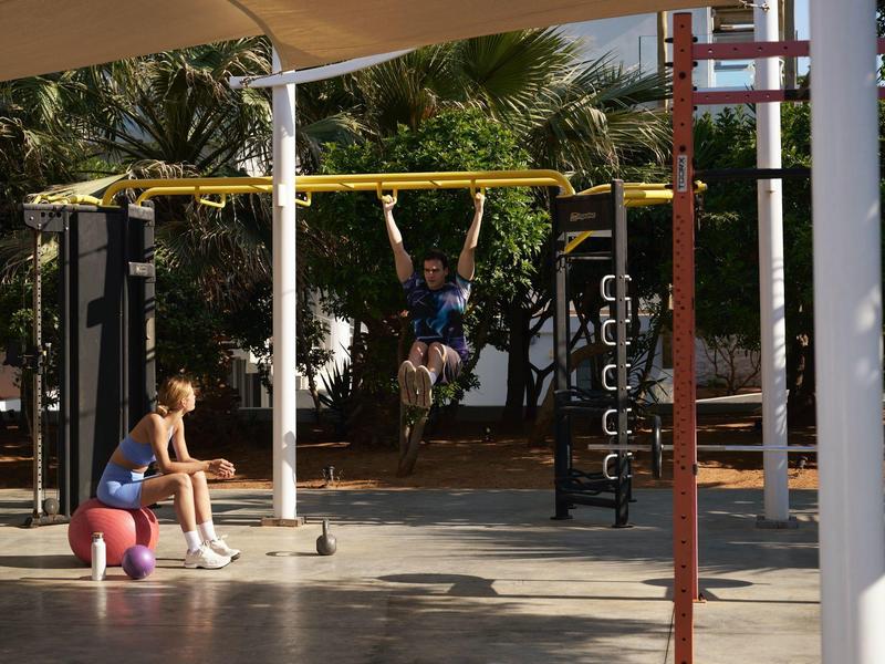Bambini giocano in un'area giochi all'aperto sotto un riparo, circondati da palme.
