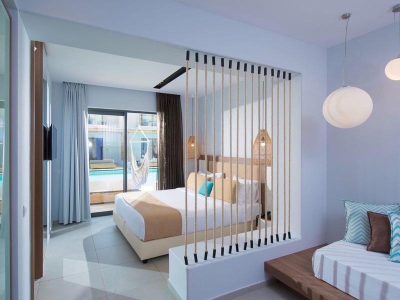 Camera d'hotel moderna con letto matrimoniale, separé a listelli, divano e vista piscina.