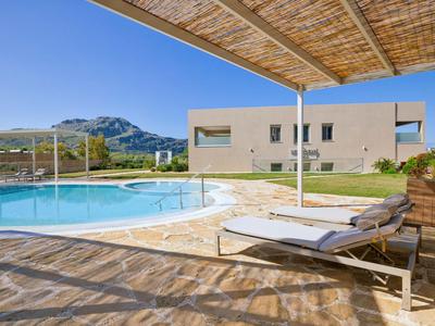 Area piscina moderna con lettino, ombra e casa sullo sfondo sotto un cielo blu.